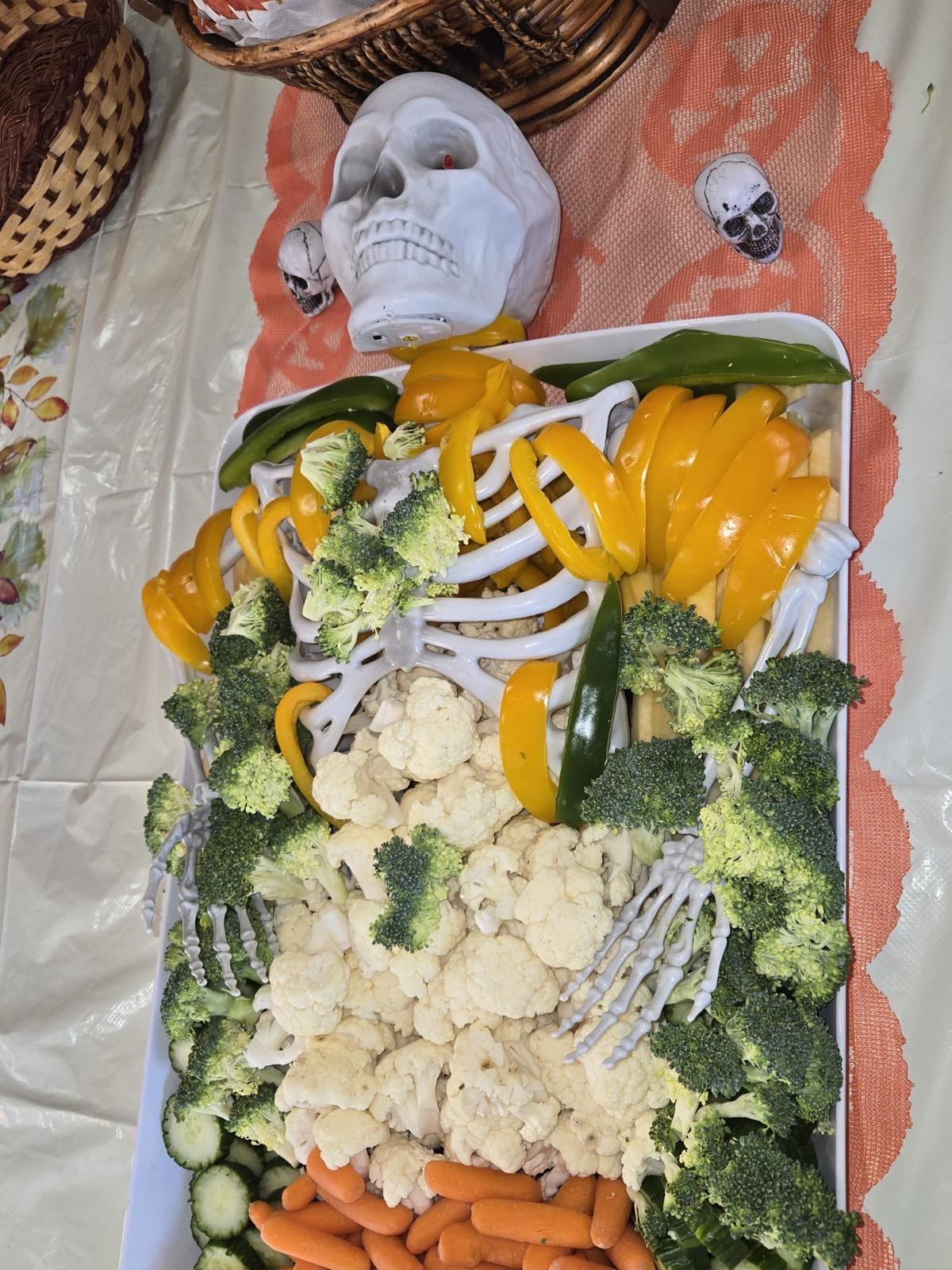 A decorative skeleton surrounded by broccoli, cauliflower, peppers, cucumber and carrots on a vegetable tray.