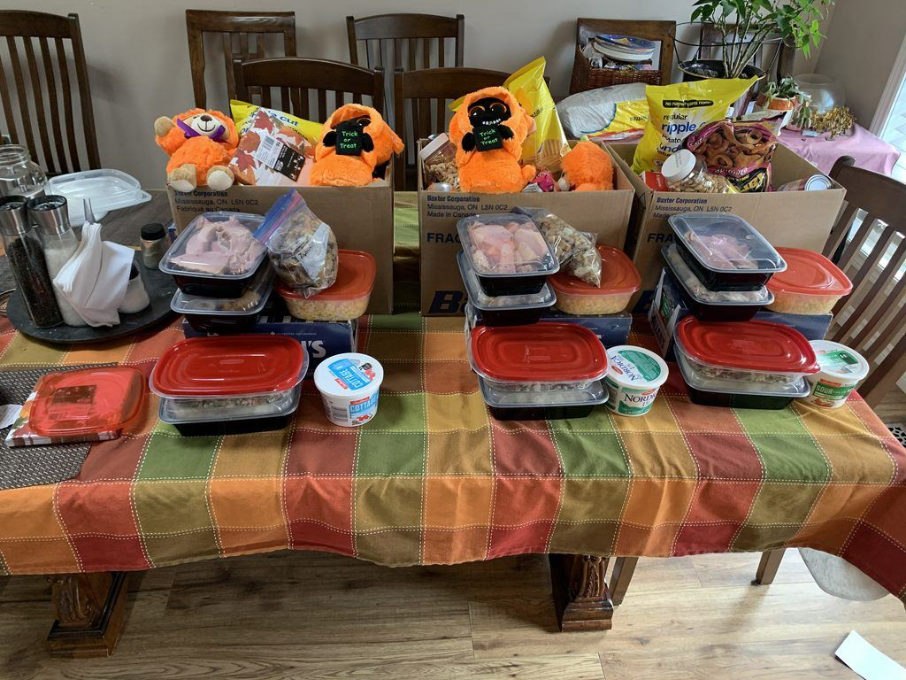 Containers of Thanksgiving food and boxes with orange Halloween toys arranged on a dining room table.
